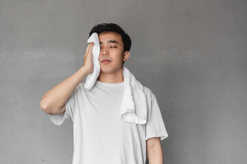 Asian man is wiping sweat in front of gray wall.