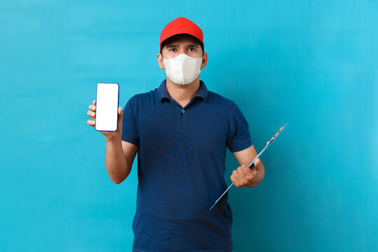 Asian delivery man wearing face mask in blue uniform, showing blank phone screen and holding a checking list