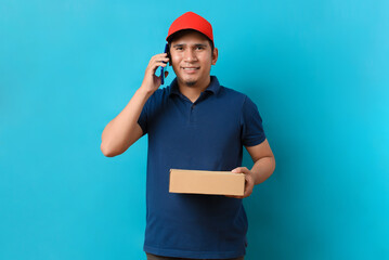 Portrait of Handsome Asian delivery man talking on the phone with a customer, isolated on blue background