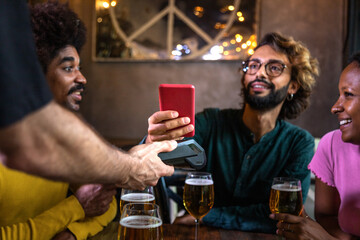 Man paying bill in a bar with phone. Friends paying round of drinks with mobile phone at pub.
