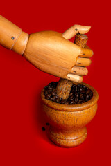Close-up of a wooden human hand grinding coffee on a red background.