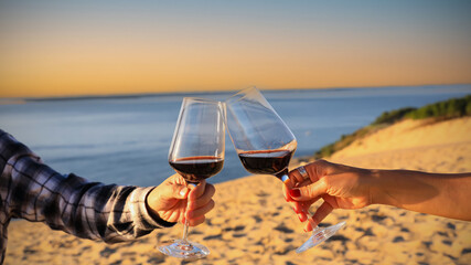 Sunset view of couple  toasting each other with wine while sitting together on a sandy beach at sunset scene mood