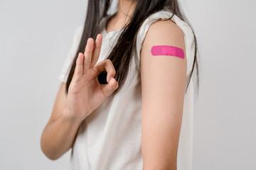 Happy young woman show ok sign after getting a vaccine. showing shoulder with bandage after...