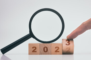 Finger flip 2023 wood block with magnifying glass on white background, newyear analysing business concept.