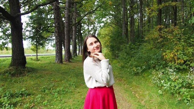Young girl corrects long dark hair. Beautiful woman in gray sweater and red skirt posing in the forest on a sunny autumn day. Walking and relaxing in the woods.