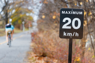 Speed limit sign, 20 kilometers per hour for bicycle lanes in park. Bike path with cyclist in autumn.