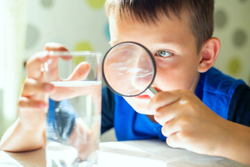 The child boy looking at water in a glass through magnifying glass