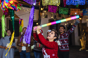 Hispanic young woman with Mexican family breaking a piñata at traditional posada party for...