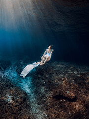 Woman freediver glides underwater. Freediving with beautiful girl in deep ocean and amazing sun rays