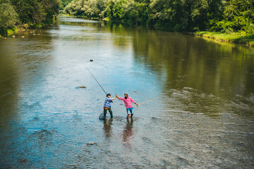 Two men friends fishing. Flyfishing angler makes cast, standing in river water. Old and young fisherman.