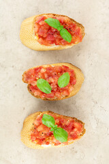 Crispy bruschetta with tomatoes, fresh basil and olive oil on a beige background, top view. Close-up.