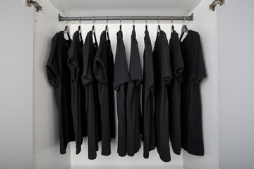 black t-shirts hang on a clothes rail in a white wardrobe. all t-shirts are the same color and size...