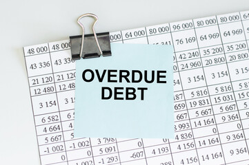 a white card with overdue debt text stands on paper clips on a desk against the light blue...