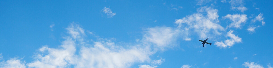 The passenger airplane is flying far away in the blue sky and white clouds. Plane in the air. International passenger air transportation. Banner or header - obrazy, fototapety, plakaty