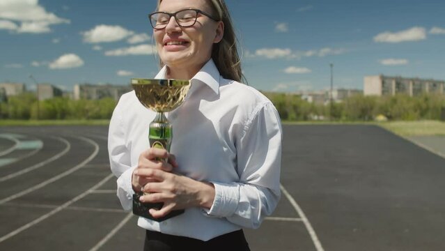 Young caucasian woman recieving an award cup at corporate event, smiling and jumping with happiness. Beautiful woman emotionally rejoice after awarding for success at work