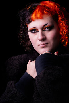 Portrait with black background of a young transgender woman with dyed orange hair.