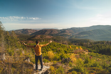 Fototapeta premium Enthusiastic traveller stands on a rock and looks down into the valley. Happy to have reached his goal. Pumping energy for the next journey. Horni Lomna, Beskydy mountains, Czech republic