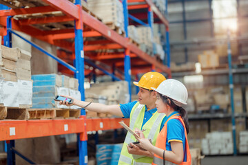 Asian engineer in helmets order and checking goods and supplies on shelves with goods background in warehouse.logistic and business export ,Warehouse worker checking packages on shelf in a large store