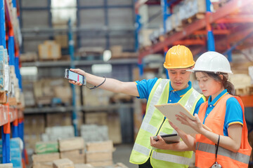 Asian engineer in helmets order and checking goods and supplies on shelves with goods background in...
