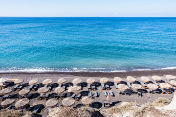 Beautiful sea view of Santorini island from a hill with sand beds and umbrellas on the beach