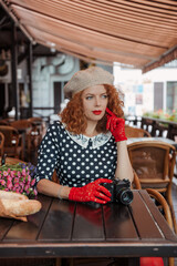 A woman in a beret and vintage dress holds a camera in her hands and takes shoots