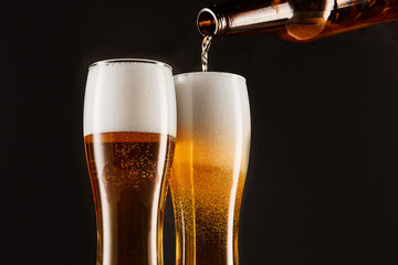 Pouring beer into glasses from bottle on dark.