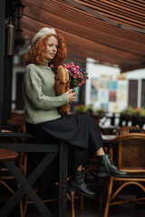 Fototapeta na wymiar Woman portrait in a beret sweater holding a bouquet of flowers of the restaurant background 