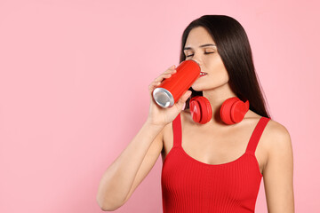 Obraz premium Beautiful young woman with headphones drinking from tin can on pink background. Space for text