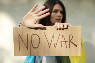 Sad woman holding poster with words No War and showing stop gesture near light wall, focus on hands
