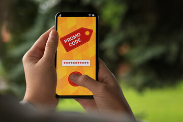 Woman activating promo code on smartphone against blurred background, closeup. Space for text