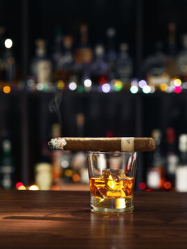 close up view of glass of burbon with cigar on top on color back. 