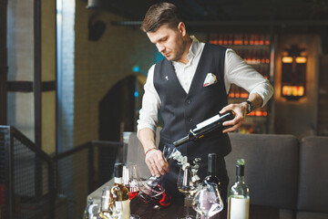 Sommelier pouring wine into glass from decanter. Male waiter