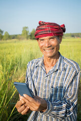 Asian man farmer with hand holding smart phone standing in rice farm, cash subsidy concept