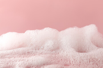 Fluffy bath foam on pink background, closeup. Care product