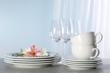 Glasses and clean dishware with flowers on grey marble table
