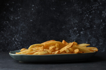 Plate of tasty french fries on black table