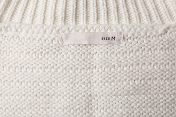 Clothing label on beautiful beige garment, top view