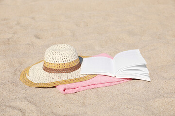 Fototapeta na wymiar Open book, hat and pink towel on sandy beach