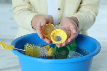 Woman holding baby bottle nipples above basin with water, closeup. Washing dishes