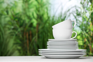 Set of clean plates and cups on white table against blurred background, space for text