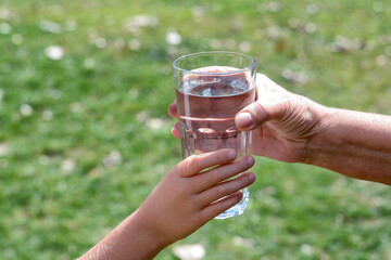 Child giving glass of water to elderly woman outdoors, closeup