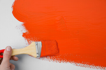 Man applying orange paint with brush on white background, closeup