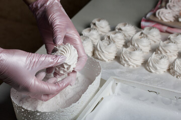 Homemade zephyr. White tray with marshmallows. A woman sprinkles marshmallows with dextrose.