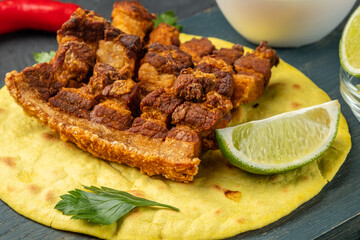 Crispy appetizer of pork belly with lime lies on a tortilla, close-up.