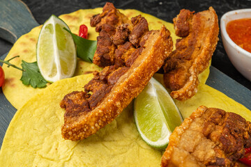 Slices of fried pork with a crispy crust on a tortilla close-up, served on a tortilla with lime.