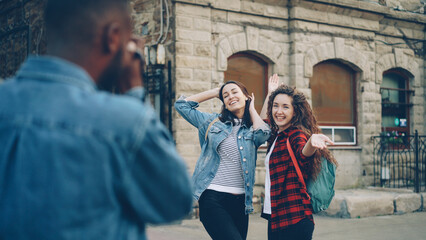 African American man tourist is taking pictures of his pretty female friends posing for camera. Tourism, photography and youth concept.