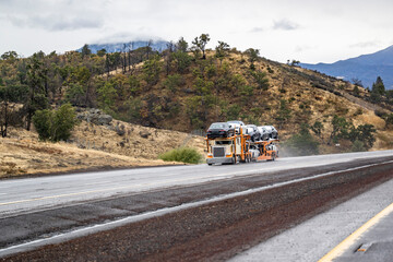 Beige and orange big rig car hauler semi truck transporting cars on two level modular semi trailer...