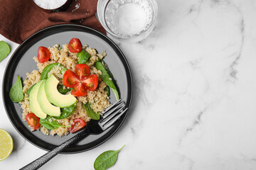 Delicious quinoa salad with tomatoes, avocado slices and spinach leaves served on white marble...