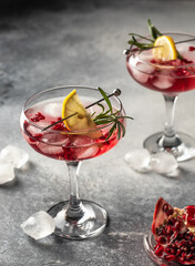 Two glasses of Pomegranate Christmas iced cocktail with rosemary and lemon on gray background . Xmas drink party concept, menu