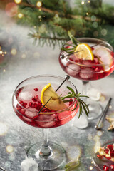 Pomegranate Christmas iced cocktail with rosemary and lemon on gray background with bokeh lights and fir branches. Xmas drink party concept